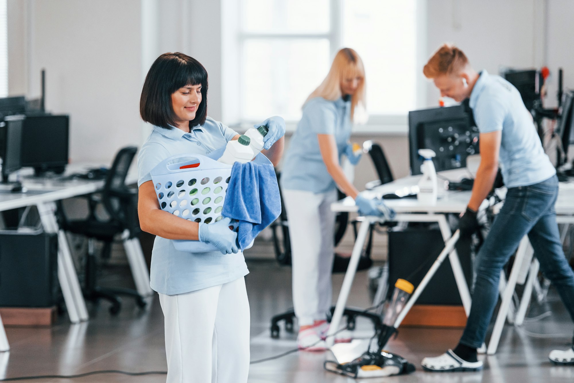 Woman with basket. Group of workers clean modern office together at daytime Woman with basket. Group of workers clean modern office together at daytime